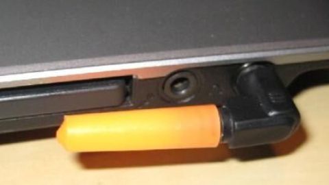 Notebook mit eingestecktem orangefarbenem Audiostecker auf einem Tisch, um laute Töne zu vermeiden.