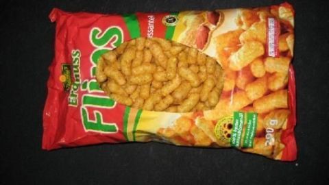 Eine geöffnete Tüte Erdnussflips liegt auf einem dunklen Tisch. Text auf der Verpackung: "Erdnuss Flips".