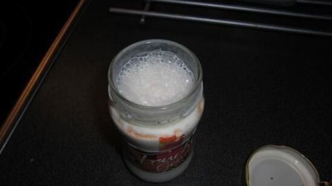 Ein Marmeladenglas steht offen auf einer Küchenarbeitsplatte, gefüllt mit einem schaumigen Milchshake.