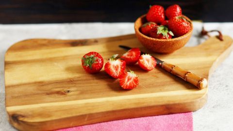 Mit diesem Tipp rutschen die Bretter nicht mehr weg bei der Arbeit weg. Ein Holzbrett liegt auf einer Arbeitsfläche, während frische Erdbeeren und ein Messer darauf liegen. Ein Schüsselchen mit Erdbeeren steht daneben.