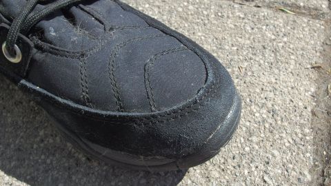Ein schwarzer Schuh mit sichtbaren Salzrändern liegt auf einem grauen, steinernen Untergrund in einem sonnigen Umfeld.