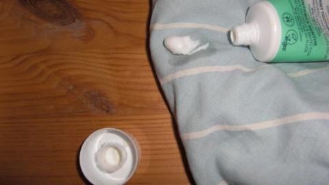 Eine Zahnpastatube steht auf einem Holztisch, während Zahnpasta auf ein Tuch gedrückt wird, um Wasserflecken zu entfernen.