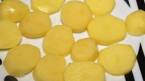 Scheiben von geschälten Kartoffeln liegen auf einem weißen Teller, bereit zur Zubereitung für Kartoffelgratin.