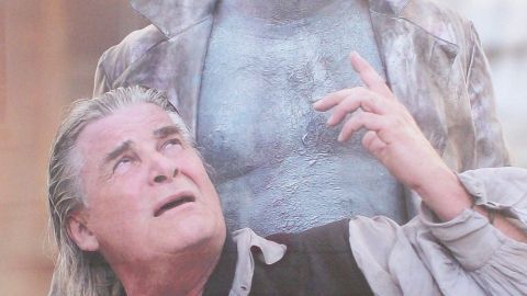 Ein Schauspieler zeigt Emotionen, während ein blauer Charakter ihn ausdrucksvoll anblickt; ihre Umgebung scheint eine Theateraufführung zu sein.