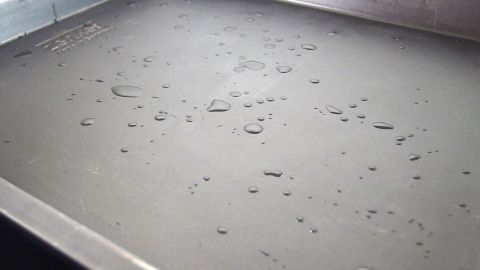 Mit ein paar Tropfen Wasser auf dem Backblech rutscht das Backpapier nicht mehr. Ein Backblech mit Wassertröpfchen wirkt rutschfest, bereit für das Platzieren von Backpapier für beste Ergebnisse.