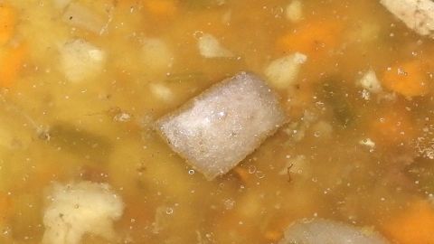 Eine goldene Bratensoße ohne Mehl bindet, mit Gemüse und Brühewürfeln sichtbar in der flüssigen Mischung.