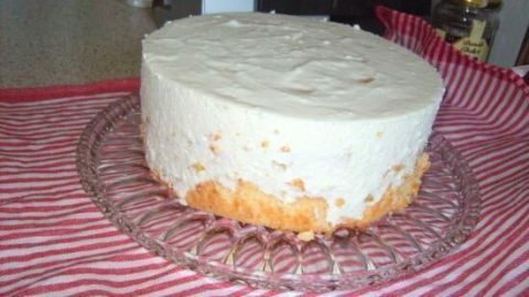 Eine Käse-Joghurt-Sahnetorte steht auf einem klaren Teller, umgeben von einem rot-weiß gestreiften Tuch in einer geschmackvollen Küche.