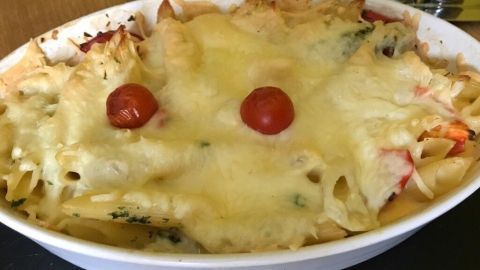 Ein Auflauf mit knuspriger Kruste und geschmolzenem Käse, garniert mit Kirschtomaten, auf einem dunklen Tisch serviert.
