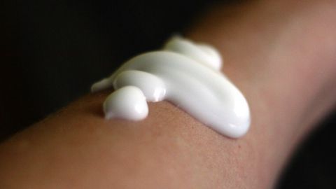 Eine handvoll Sonnenschutzmittel mit hohem UV-Schutz wird auf die Haut eines Arms aufgetragen, um vor Sonne zu schützen.