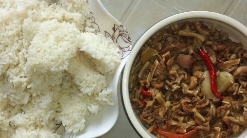 Klebereis liegt links auf einem Teller, w&auml;hrend daneben eine Sch&uuml;ssel mit w&uuml;rzigem chinesischem Gericht und roten Chilischoten steht.