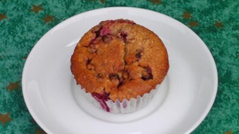 Auf einem weißen Teller liegt ein saftiger Muffin mit Johannisbeeren, umgeben von einem grünen Hintergrund mit Sternen.