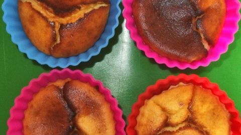 Käsekuchen-Masse in Muffinförmchen füllen: In 20 Minuten sind kleine Käsekuchen fertig. Käsekuchen in Förmchen zeigt vier kleine, gebräunte Küchlein in bunten Silikonformen auf einer grünen Unterlage.