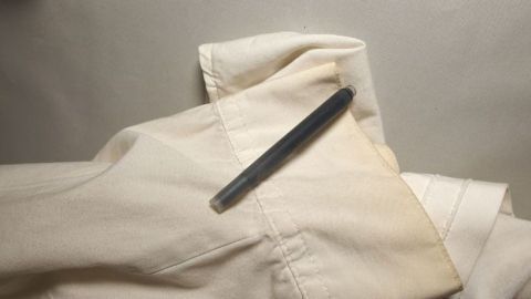 Ein Stift liegt auf vergilbter weißer Wäsche, die anscheinend für die Behandlung mit Tinte vorbereitet ist.
