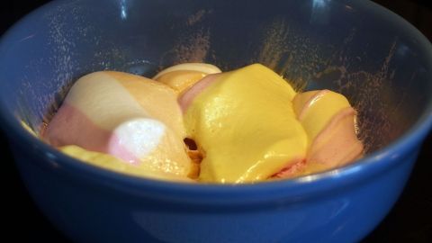 In einer blauen Schüssel schmelzen bunte Marshmallows in der Mikrowelle und bilden eine cremige, klebrige Masse.