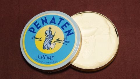 Eine runde Dose mit Penatencreme steht offen auf einem braunen Untergrund, bereit zur Anwendung bei kleinen Wunden.