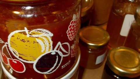Ein Glas Marmelade mit buntem Obstlabel steht in der Mitte, umgeben von weiteren Marmeladengläsern und einem Holzuntergrund.