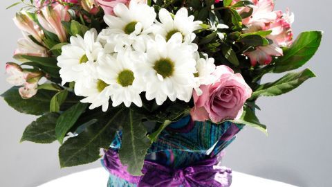 Ein bunter Blumenstrauß in einem dekorativen Stoff, der auf einem Tisch steht, sorgt für eine fröhliche Atmosphäre.