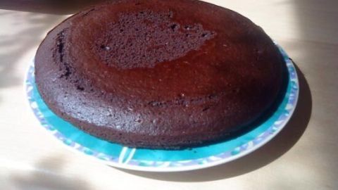 Ein runder Schokokuchen liegt auf einem bunten Teller auf einem Holztisch, beleuchtet von Sonnenlicht.
