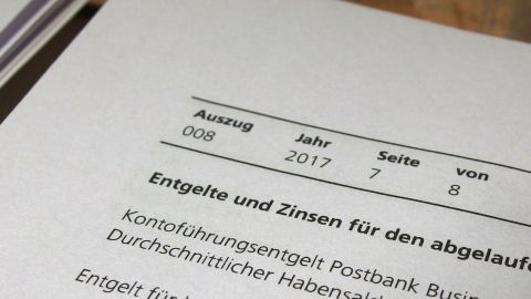 Ein Dokument zeigt Informationen über Kontoführungsgebühren und Zinsen, datiert auf 2017, in einem Büro-Setting.