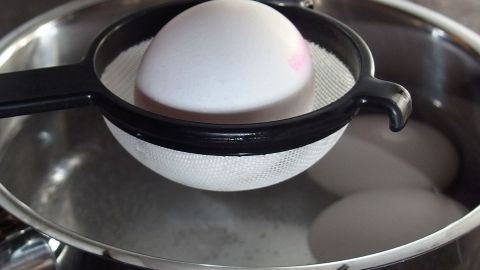 Legt man ein gesprungenes Ei in ein Sieb und hält dieses etwa 1 Minute über den Wasserdampf, erstarrt dadurch das Eiweiß entlang der Schadstelle, sodass keine Auslaufgefahr mehr entsteht. Ein Ei liegt in einem Sieb über einem Topf mit kochendem Wasser, während andere Eier im Wasser schwimmen.