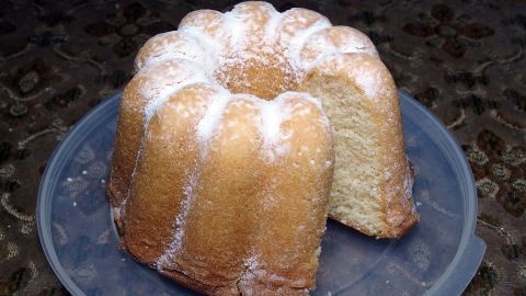 Ein Zitronenkuchen steht auf einem Teller, handlich geschnitten und leicht mit Puderzucker bestäubt.