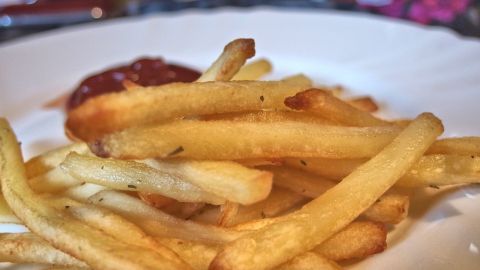 Knusprige Pommes liegen auf einem weißen Teller, umgeben von einem Hauch von Ketchup und einer farbenfrohen Tischdecke.