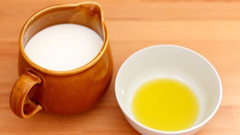 Eine braune Kanne mit Milch steht neben einer kleinen weißen Schüssel mit goldenem Öl auf einem Holzuntergrund, ideal für die Pflege trockener Haut.