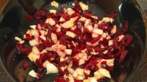 Ein bunter Salat aus fein gehackter roter Beete und Äpfeln liegt in einer dunklen Schüssel auf einem Tisch.