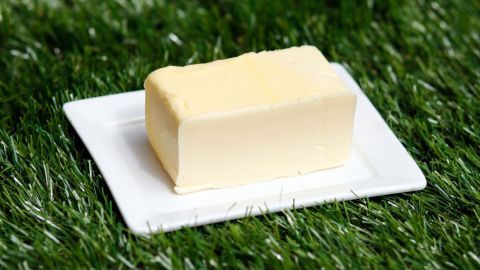 Ein Stück Butter liegt auf einem weißen Teller, der auf grünem Gras platziert ist.