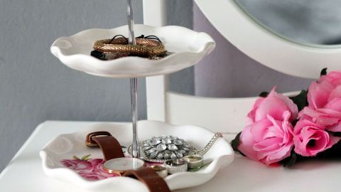 Eine Etagere präsentiert Schmuck auf zwei Etagen, dekoriert mit Rosen und spiegelt sich in einem eleganten Rahmen.