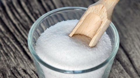 Ein Glas mit Salz und einem Holzlöffel steht auf einem rustikalen Holztisch, ideal für Hausmittel bei kleinen Verbrennungen.