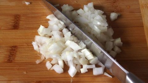 Kleine, gewürfelte Zwiebeln liegen auf einem Holzbrett, während ein scharfes Messer sie zerteilt, um ein Gericht zuzubereiten.