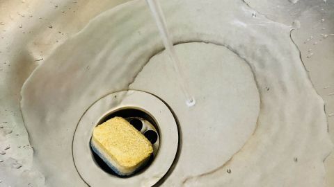 Ein Waschbecken wird mit Wasser gereinigt, während ein Geschirrtuch im Abfluss liegt und dort sauber wird.