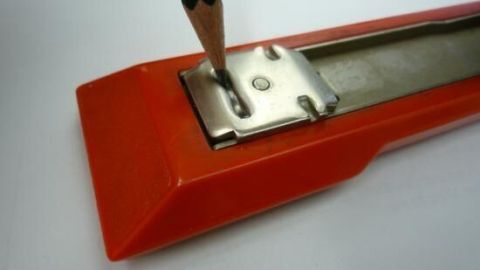 Ein orangefarbenes Heftklammergerät wird mit einem Bleistift in der Nähe der Klammerplatte gehalten, bereit zum Tunen.