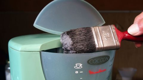 Eine Kaffeemaschine wird von innen mit einem Pinsel gereinigt, um Ablagerungen zu entfernen und ihre Leistung zu optimieren.