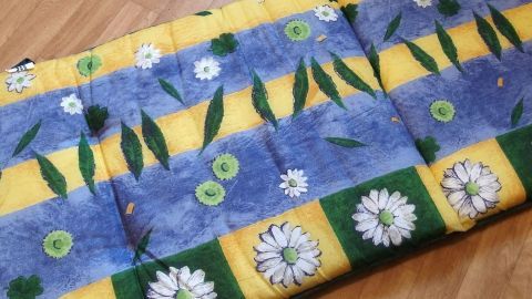 Ein Sitzkissen mit buntem Baumwollbezug liegt auf einem Holzboden, zeigt Blumenmuster und wartet auf die Reinigung von Stockflecken.