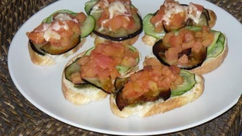 Bruschetta auf einem Teller, belegt mit Tomaten und Auberginen, liegt auf einem geflochtenen Tischset.
