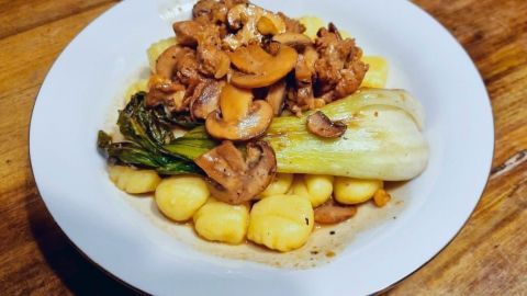 Saftiges Rinderfilet liegt auf cremigen Steinpilzgnocchi, umgeben von gedünstetem Fenchel, auf rustikalem Holz.
