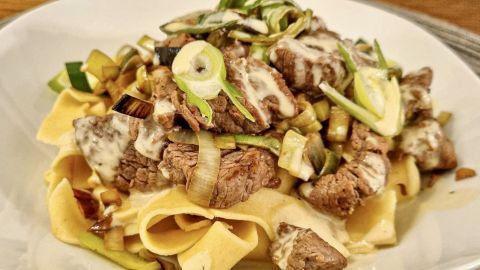 Tagliatelle liegen in einer Schüssel und sind mit zarten Filetspitzen sowie einer cremigen Sauce und Lauch garniert.