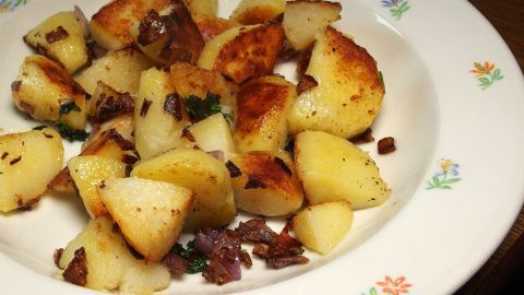In einer Schüssel liegt goldbraun gebratener Kartoffelgulasch, umgeben von einer bunten Blume-Musterkante.