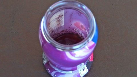 Ein Glas mit Resten von Joghurt steht auf einem Tisch, die lilafarbene Farbe zeigt, dass wenig Inhalt übrig ist.