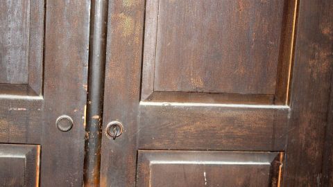 Mit warmem Bier kann man dunkle Holztüren wieder zum glänzen bringen. Dunkle Türen aus Holz stehen nebeneinander, leicht geöffnet, und lassen schummriges Licht in den Raum strömen.