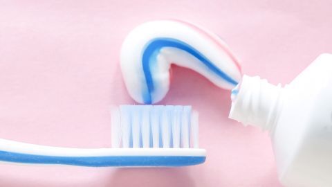 Eine Zahnbürste mit Zahnpasta steht bereit, um Selbstbräuner-Flecken auf einer pinken Oberfläche zu entfernen.