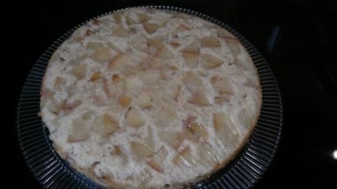 Ein Apfelkuchen liegt verkehrt herum auf einem gläsernen Teller, die Apfelstücke sind oben sichtbar und gleichmäßig verteilt.