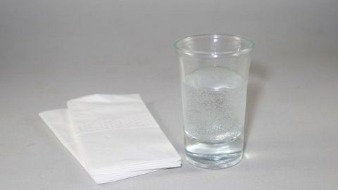 Ein Glas Wasser steht auf einem grauen Hintergrund, neben zwei weißen Servietten, bereit zur Verwendung bei Erkältung.