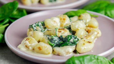 Gnocchi liegen auf einem rosa Teller, umgeben von frischem Spinat, in einer cremigen Spinatsauce.