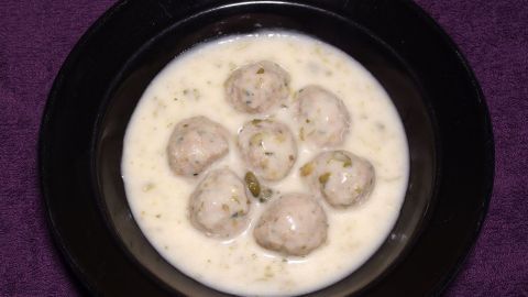Eine Schüssel mit weißen (Creme-)Suppen enthält mehrere runde Fleischbällchen und steht auf einem lila Hintergrund.
