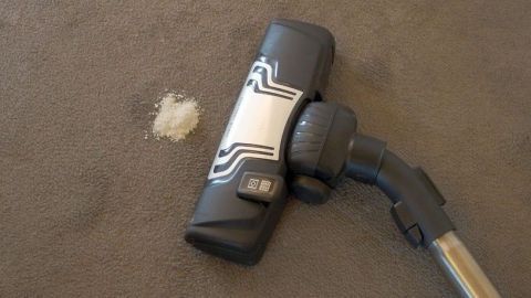 Ein Staubsauger mit einer Düse saugt Schmutz von einem Teppich auf, während ein kleiner Fleck sichtbar bleibt.