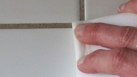 Ein Schmutzradierer reinigt Fugen, während eine Hand sanft über die Kachelverfugungen wischt, um Schmutz zu entfernen.
