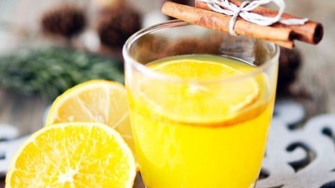 Ein warmes Glas O-Saft steht auf einem rustikalen Tisch, umgeben von frischen Zitronenscheiben und einer Zimtstange.